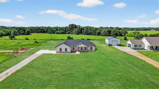 a view of an house with a big yard and large trees