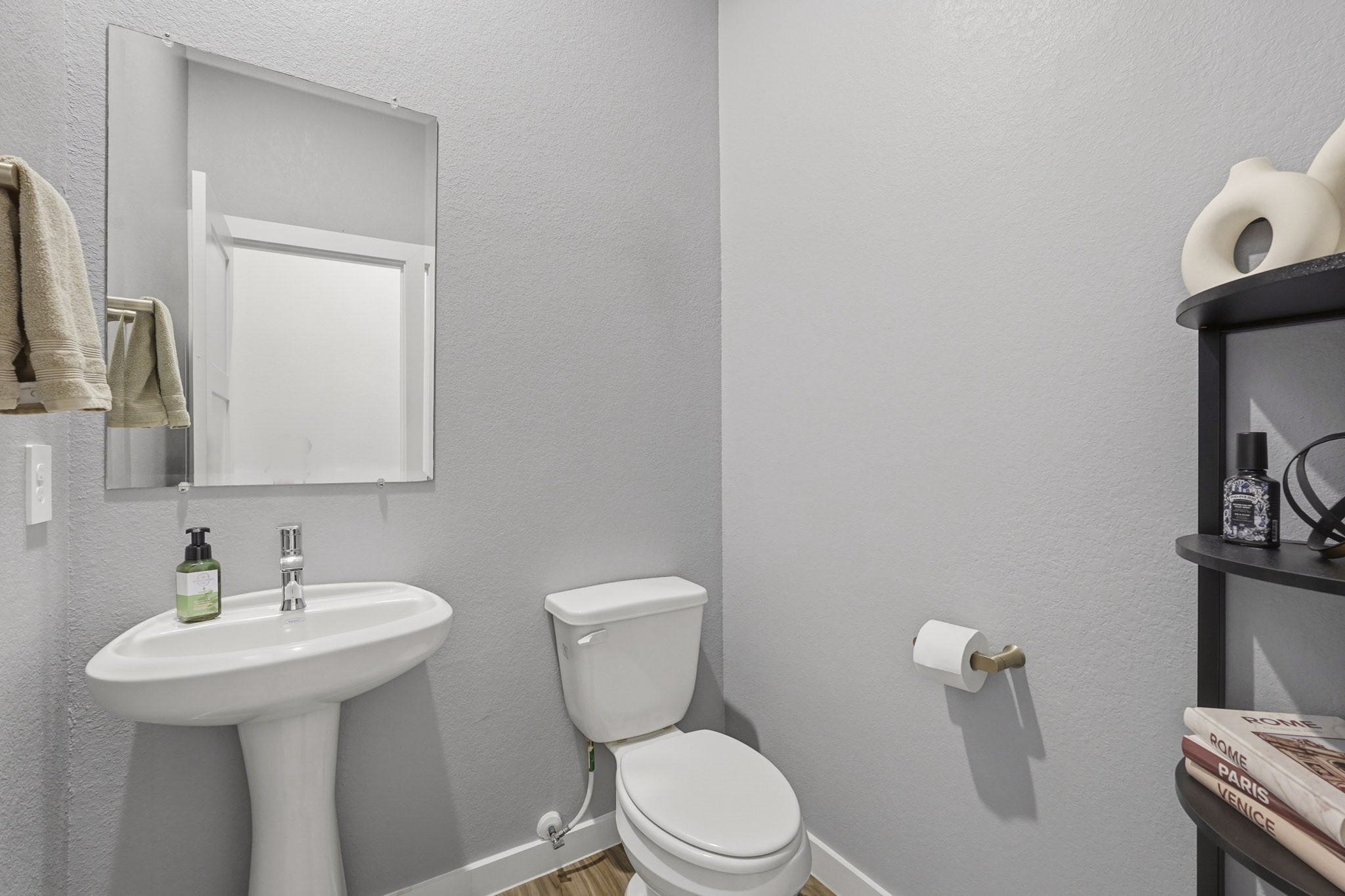 22522 Modica Rift Lane Katy, TX 77449 - Photo 32 of 38 Tucked conveniently off the main living areas, this clean and charming powder bath is ready to welcome guests with ease. A classic pedestal sink, polished chrome fixtures, and a curated shelf with stylish accents keep things simple yet intentional. Every detail — right down to the travel books and sculptural décor — shows that even the smallest spaces in this home have been thoughtfully considered.