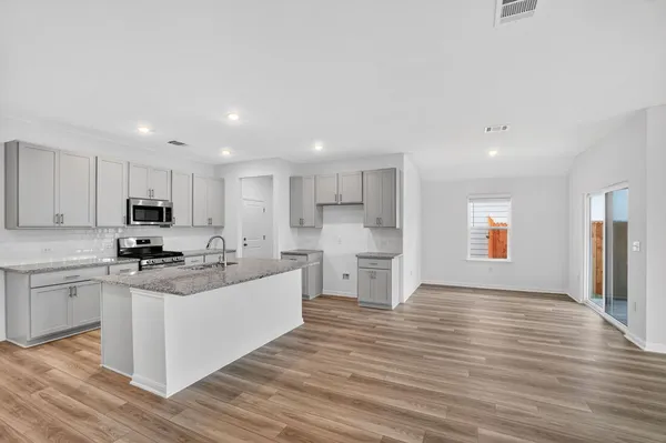 a kitchen with stainless steel appliances kitchen island granite countertop a stove top oven a sink and white cabinets