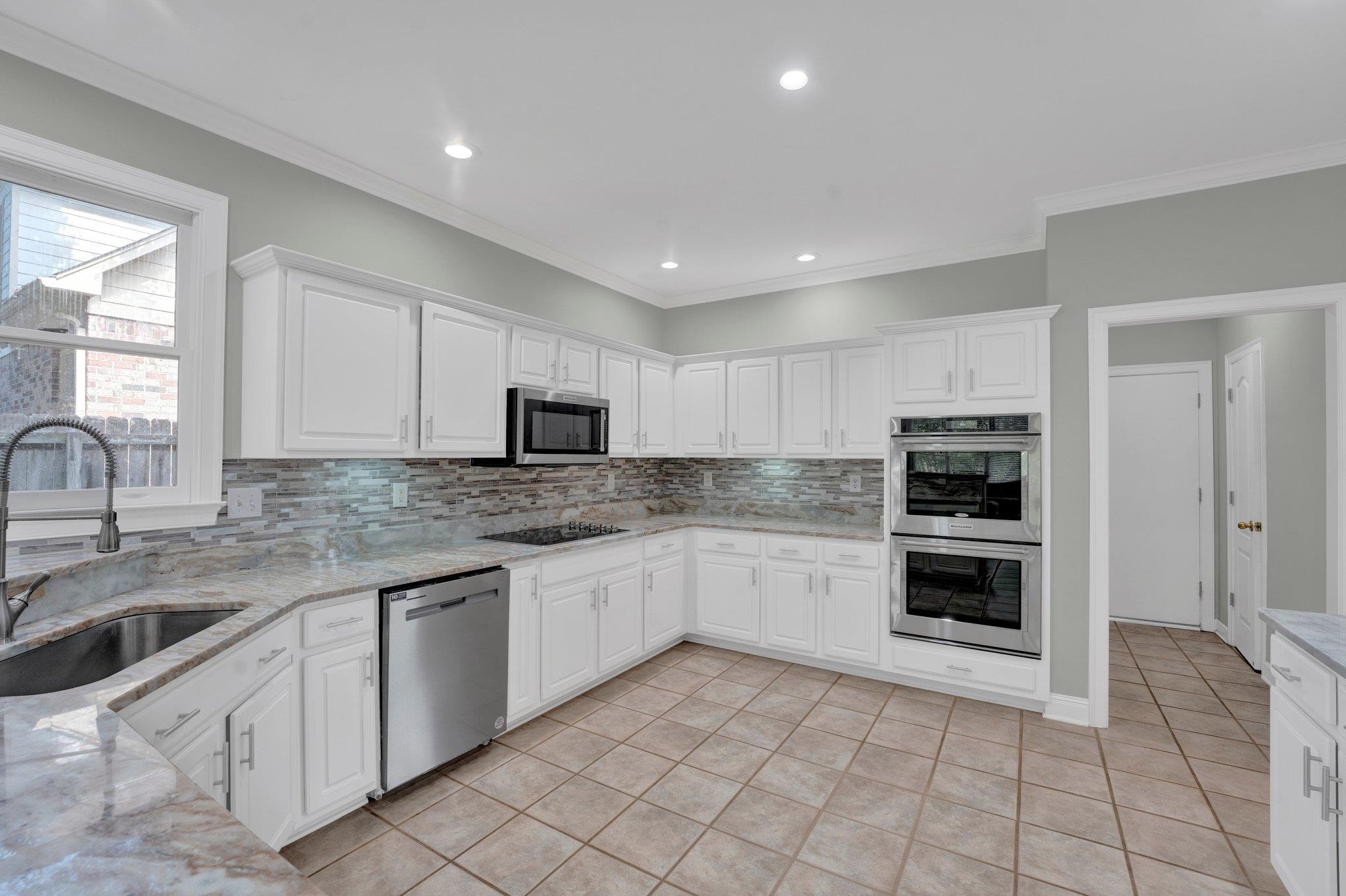 1331 Riding Brook Drive Collierville, TN 38017 - Photo 14 of 39 Kitchen with stainless steel appliances, white cabinets, sink, decorative backsplash, and light stone countertops