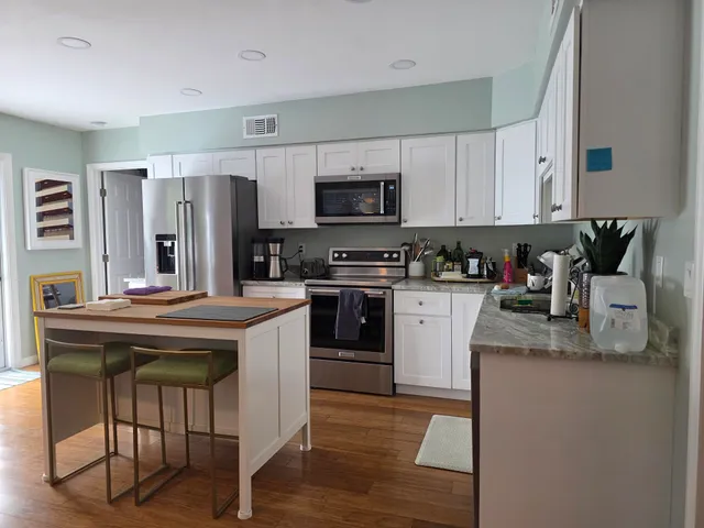 a kitchen with stainless steel appliances granite countertop a refrigerator a stove a sink dishwasher and white cabinets with wooden floor