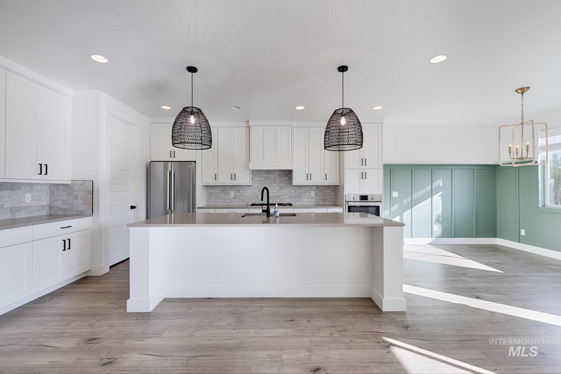 6216 South Wayland Way Meridian, ID 83642 - Photo 12 of 38 Modern kitchen featuring white cabinetry, a large central island with countertop seating, stainless steel appliances, and wood-finish flooring