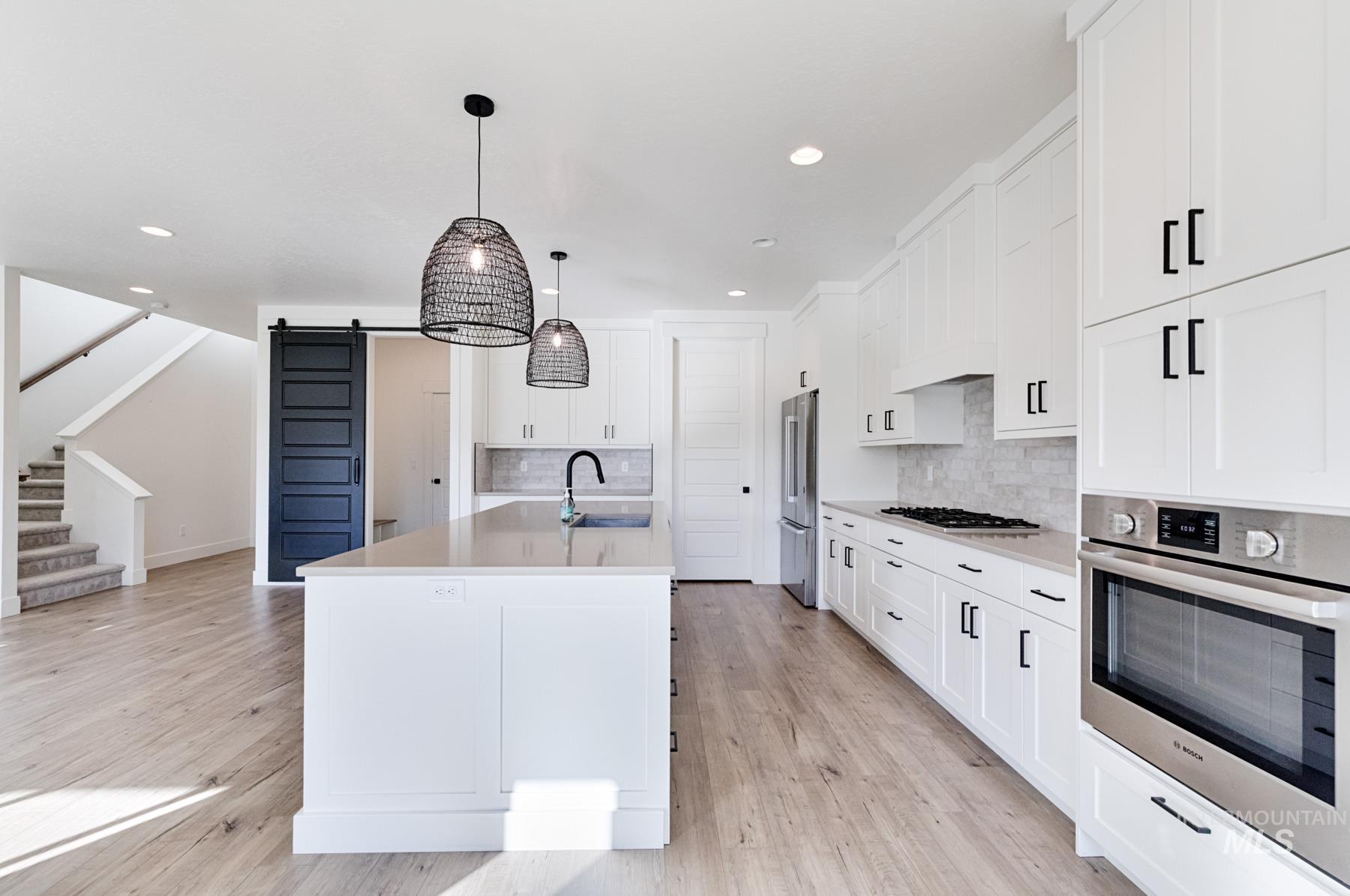6216 South Wayland Way Meridian, ID 83642 - Photo 14 of 38 Open-concept kitchen featuring white shaker cabinetry, stainless steel appliances, a light-toned backsplash, and an expansive center island with a matte black faucet