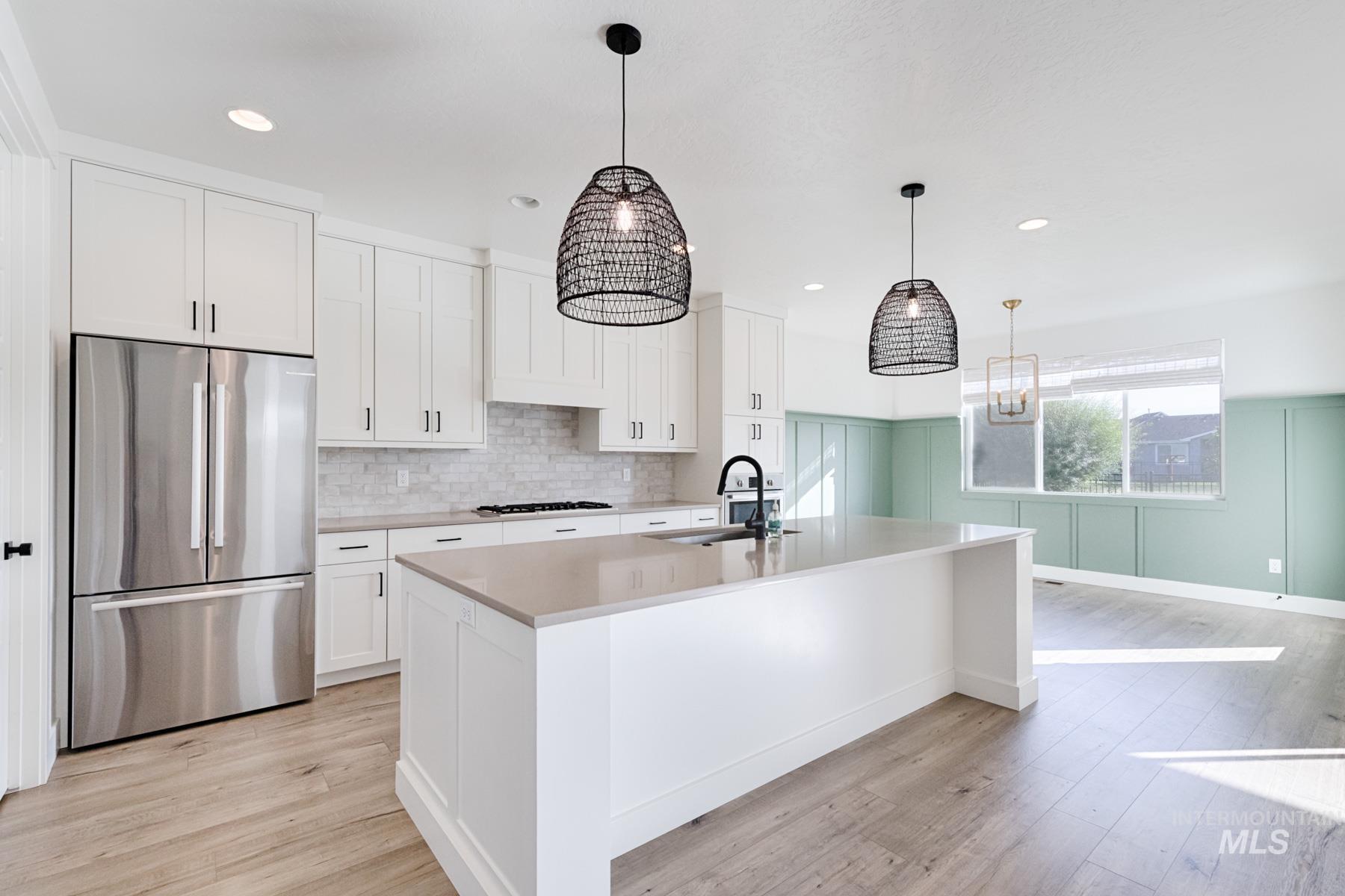 6216 South Wayland Way Meridian, ID 83642 - Photo 15 of 38 Kitchen featuring an expansive island with a light-toned countertop, white cabinetry with dark hardware, stainless steel appliances, a tile backsplash, and wood-finish flooring