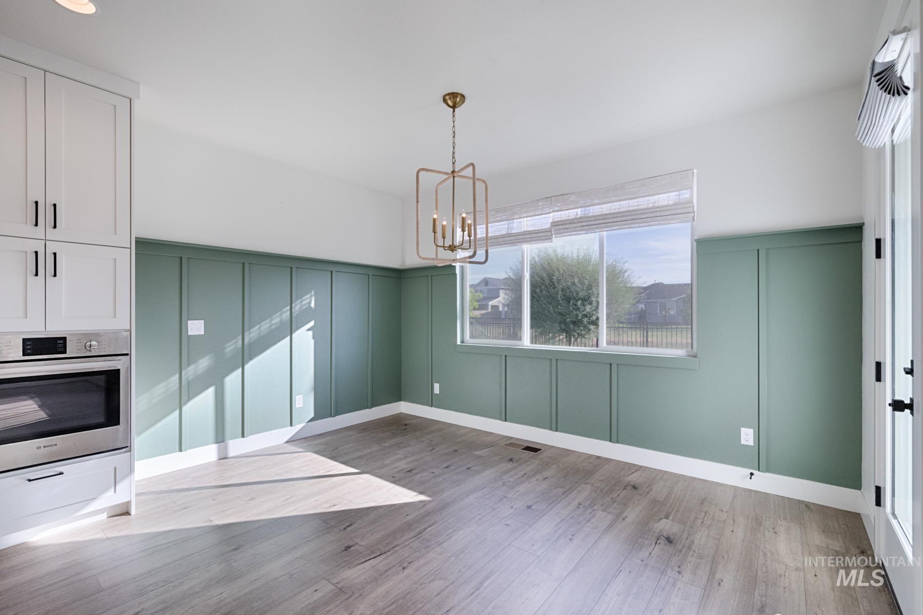 6216 South Wayland Way Meridian, ID 83642 - Photo 17 of 38 Dining area featuring wainscoting with a sage finish, large window with blinds, wood-finish flooring, and a modern geometric chandelier