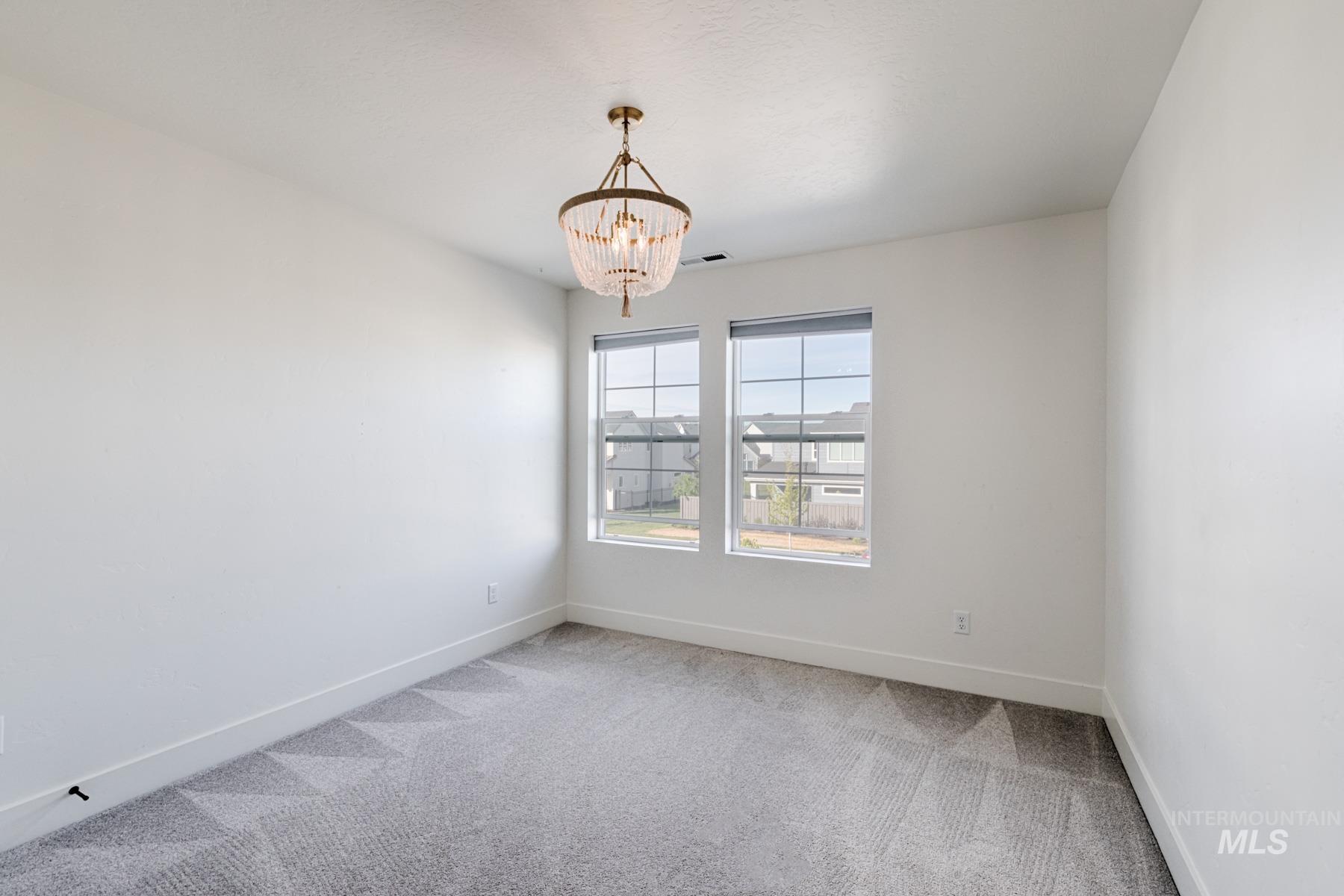 6216 South Wayland Way Meridian, ID 83642 - Photo 30 of 38 Bright interior space featuring a decorative chandelier with a beaded shade, two windows, clean white walls, and patterned carpeting