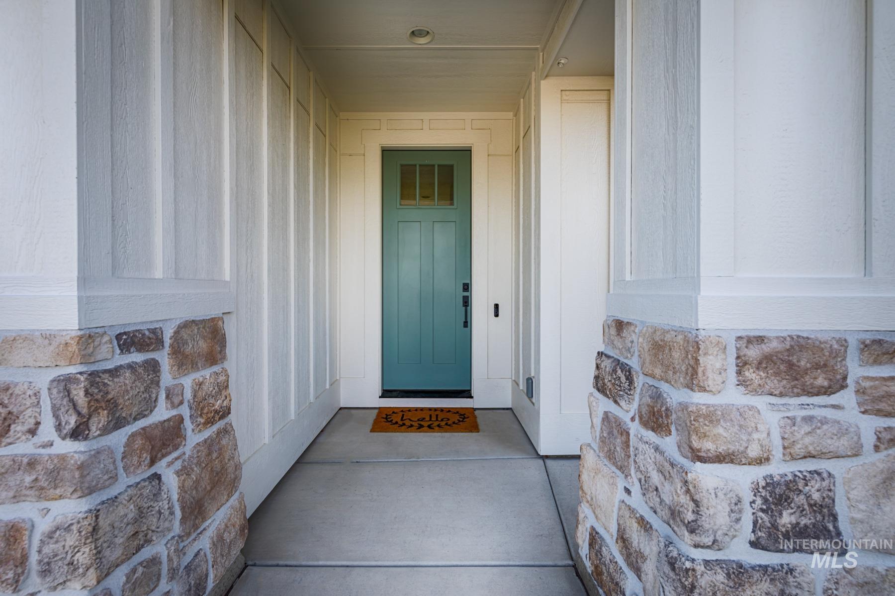 6216 South Wayland Way Meridian, ID 83642 - Photo 4 of 38 Inviting entryway featuring a teal panel door with glass inserts, board and batten siding, stone veneer accents, recessed lighting, and a concrete walkway
