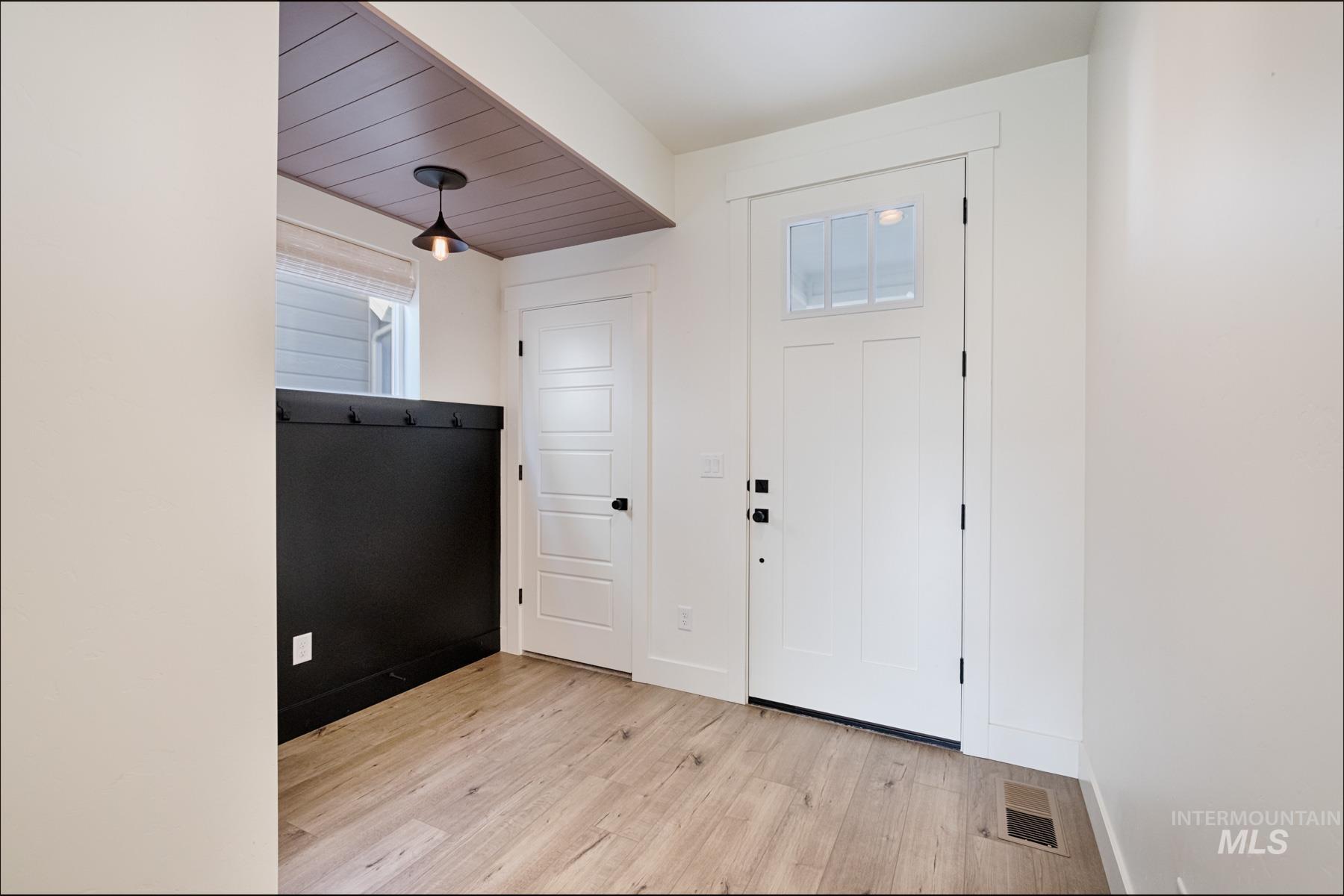 6216 South Wayland Way Meridian, ID 83642 - Photo 5 of 38 Entryway featuring a white paneled door with glass inserts, wood-finish flooring, and a contrasting dark paneled wall with integrated hooks