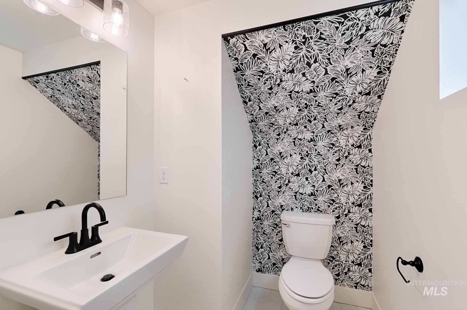 6216 South Wayland Way Meridian, ID 83642 - Photo 6 of 38 Powder room featuring a pedestal sink with a matte black faucet, a framed wall mirror, and a toilet set against a tropical-patterned accent wall