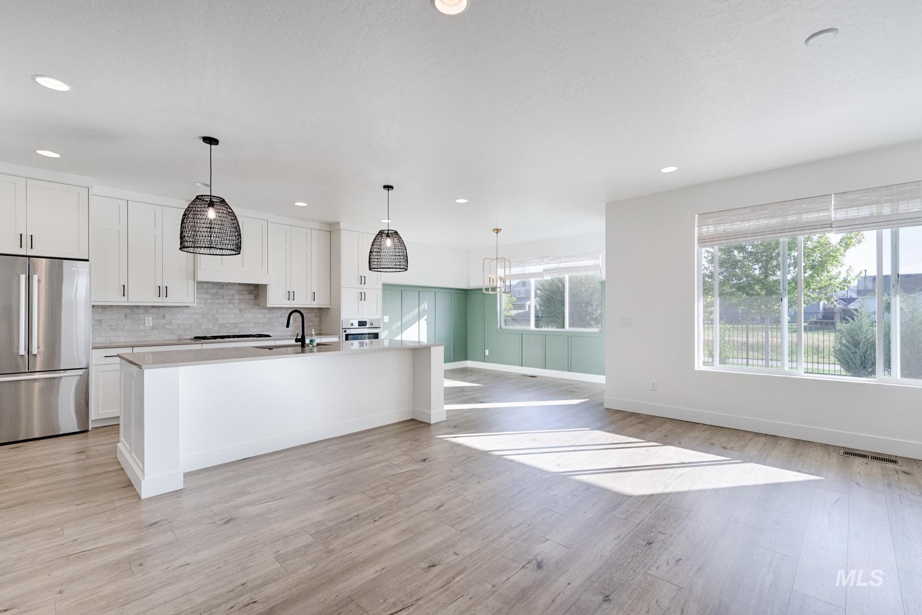 6216 South Wayland Way Meridian, ID 83642 - Photo 7 of 38 Modern kitchen featuring white cabinetry, a large center island with a sink, stainless steel appliances, and wood-finish flooring