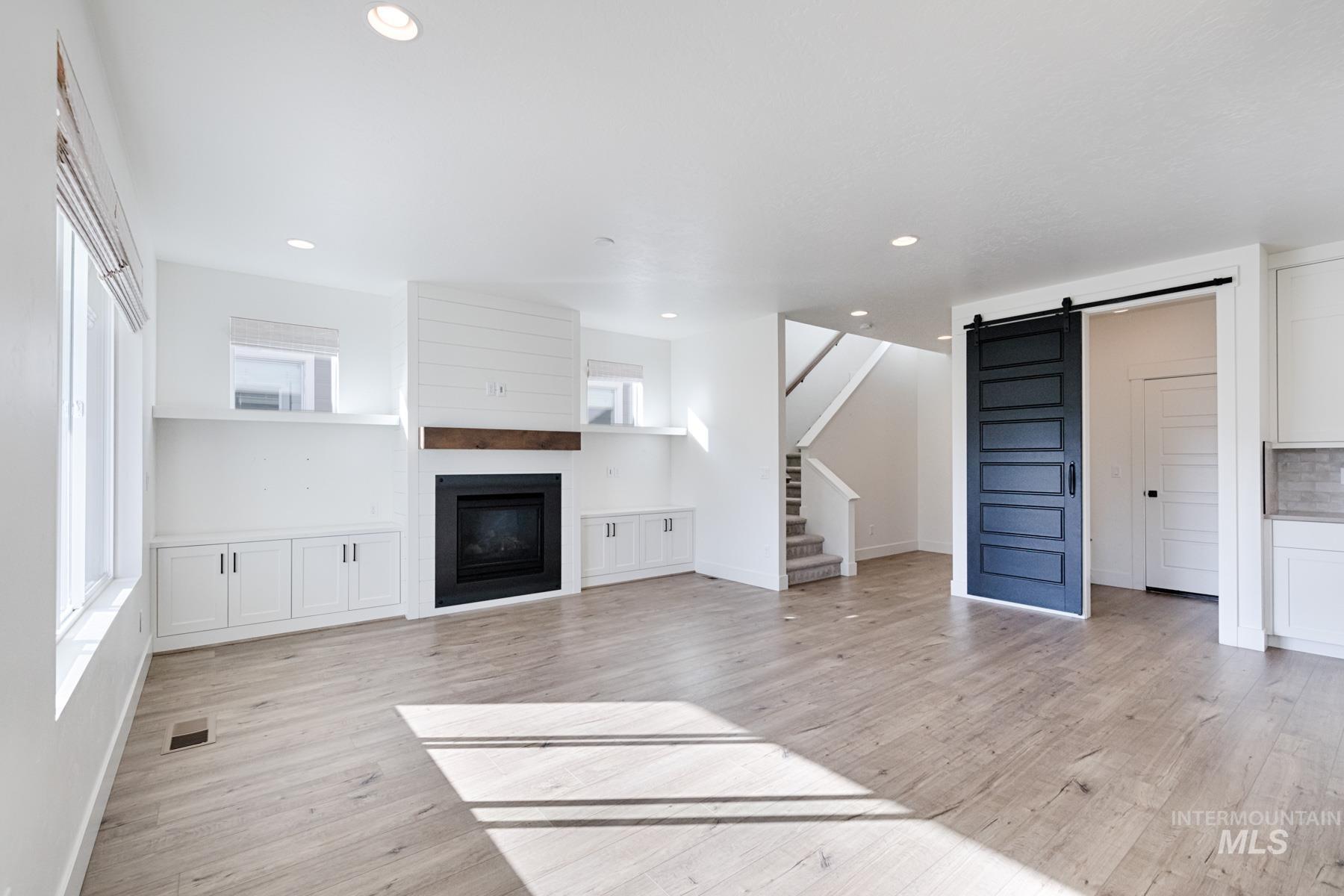 6216 South Wayland Way Meridian, ID 83642 - Photo 10 of 38 Spacious living area featuring wood-finish flooring, a contemporary fireplace with a shiplap surround and wood mantel, built-in cabinetry, recessed lighting, and a dark-paneled sliding barn door