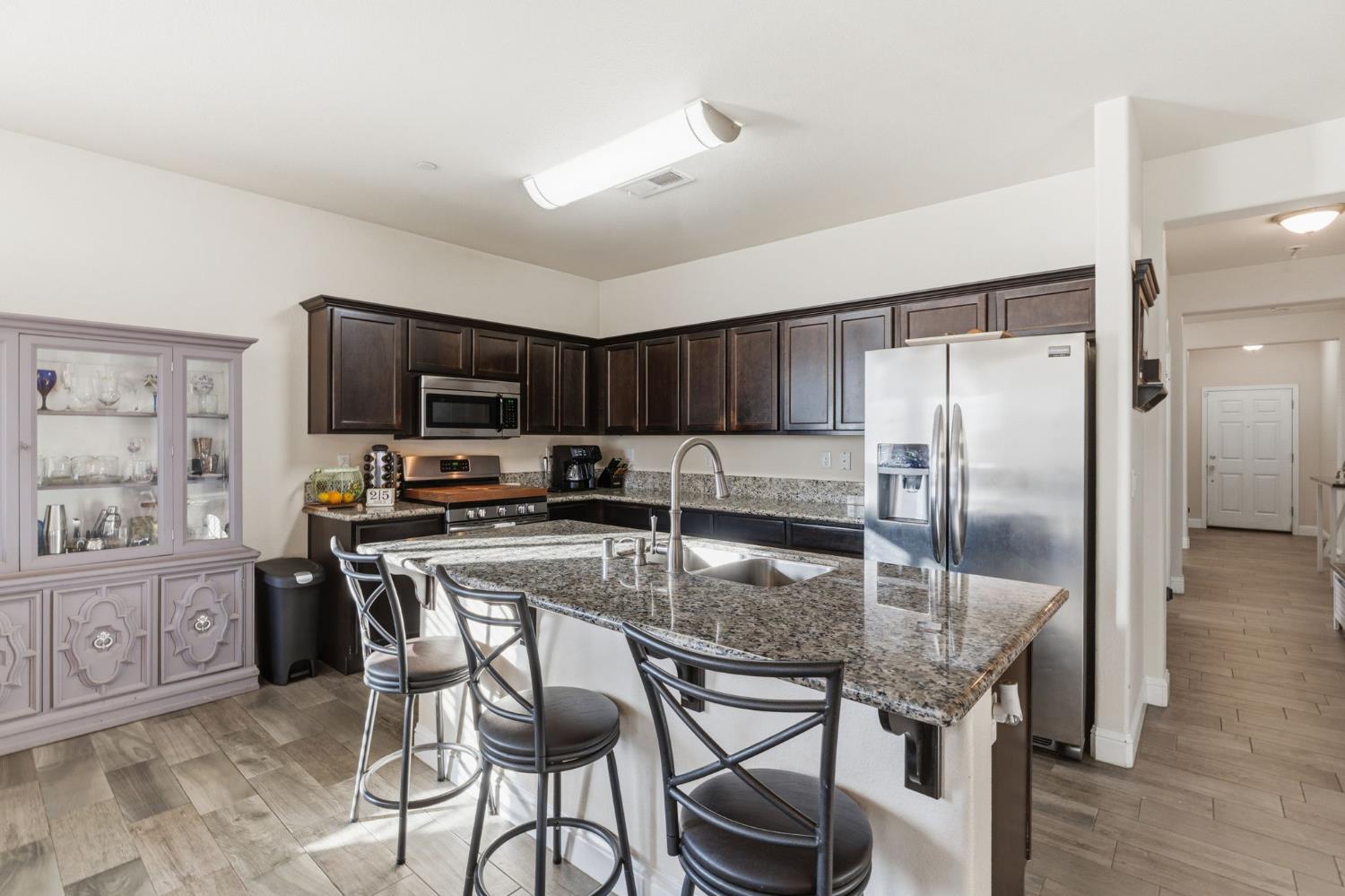 15717 West Botelho Avenue Kerman, CA 93630 - Photo 23 of 43 a kitchen with kitchen island granite countertop a refrigerator a stove a sink a dining table and chairs with wooden floor