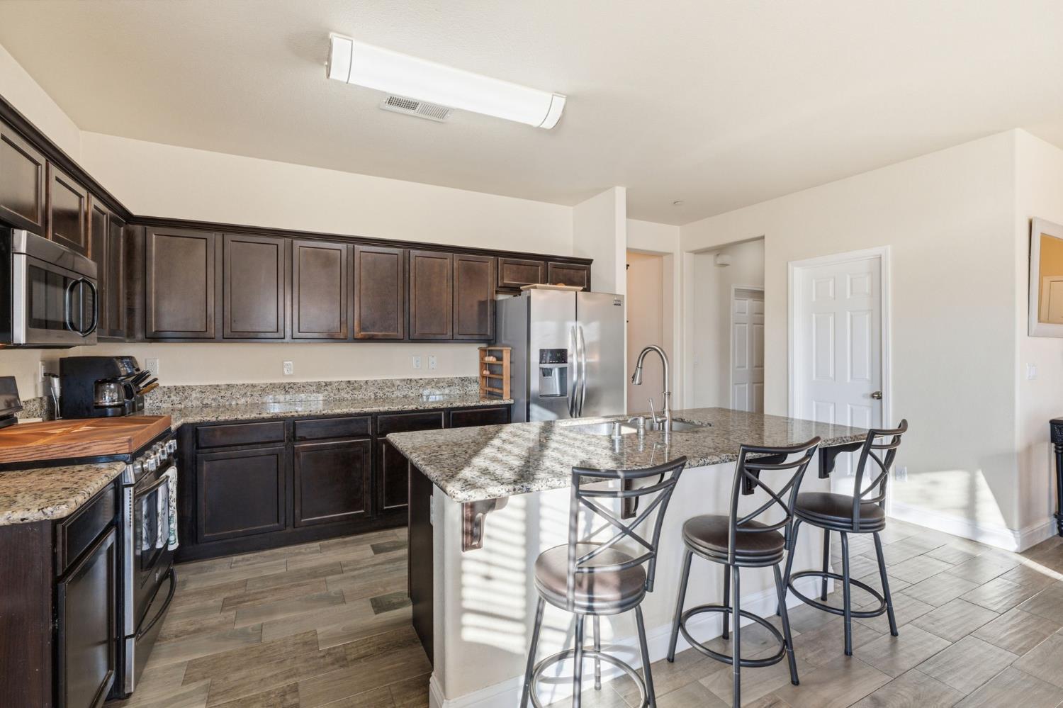 15717 West Botelho Avenue Kerman, CA 93630 - Photo 24 of 43 a kitchen with granite countertop a table chairs stove and cabinets