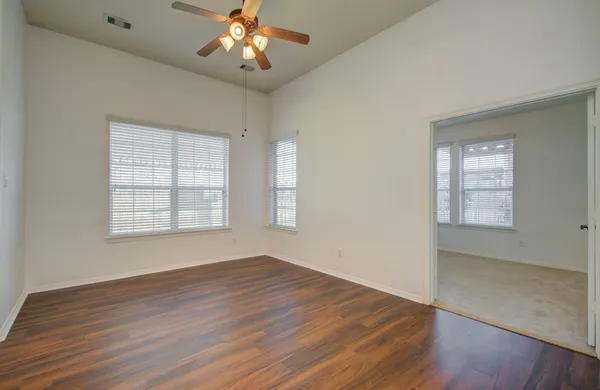 an empty room with wooden floor chandelier fan and windows