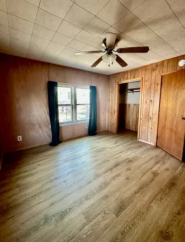 an empty room with wooden floor fan and windows