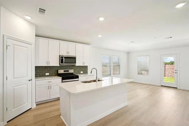 a kitchen with stainless steel appliances a stove top oven a sink a refrigerator with white cabinets