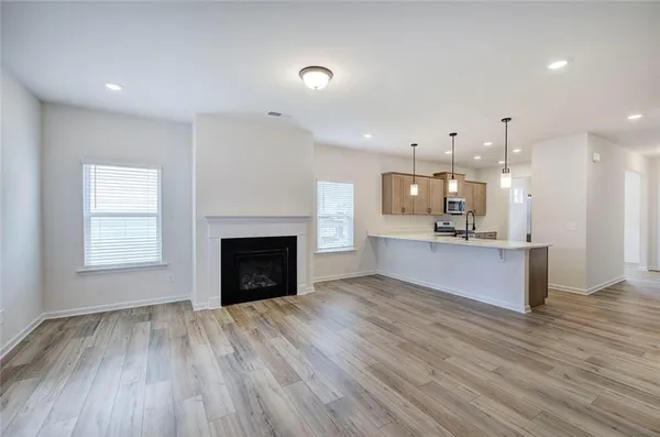 a view of a kitchen and an empty room with wooden floor and a fireplace
