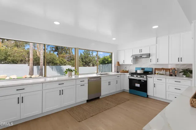 a large kitchen with granite countertop a stove top oven a sink a window and white cabinets