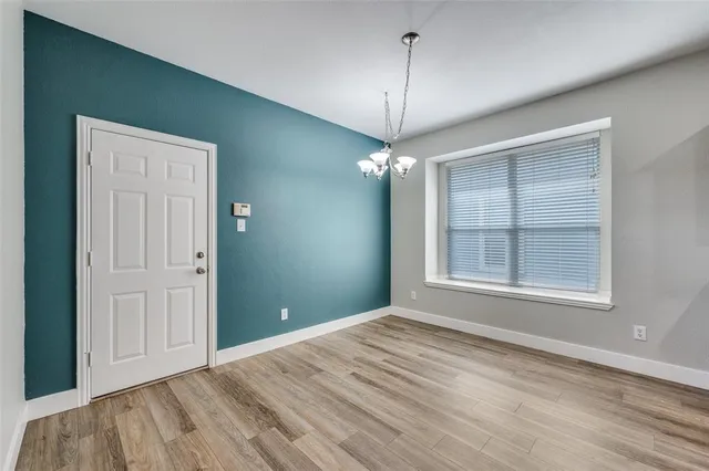 an empty room with wooden floor chandelier and windows
