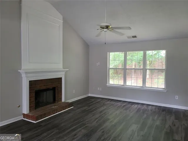 a view of an empty room with wooden floor fireplace and a window