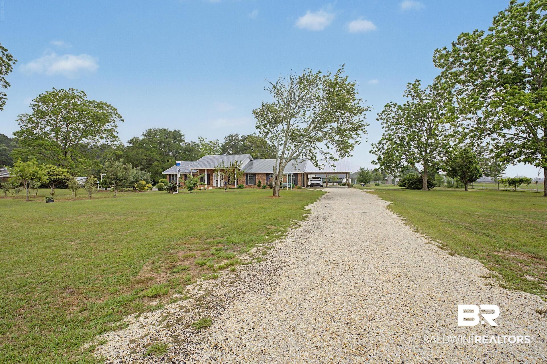 3791 Robinsonville Road Atmore, AL 36502 - Photo 6 of 47 Long gravel driveway leading to a brick residence with a covered front porch featuring white columns and a gray roof