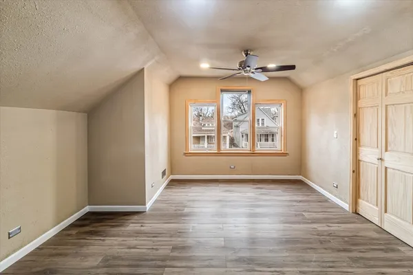 an empty room with wooden floor chandelier fan and windows