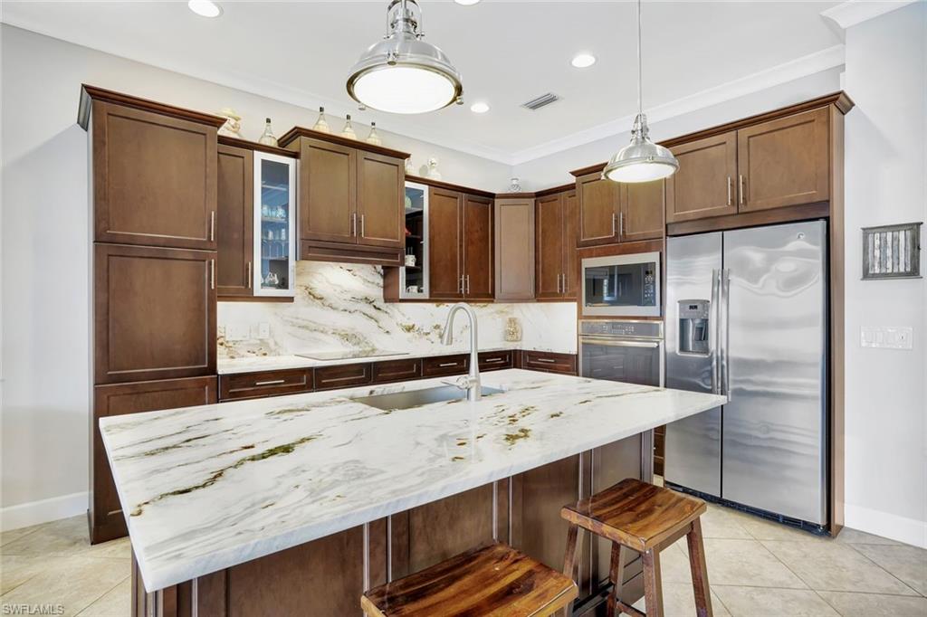 4905 Andros Drive Naples, FL 34113 - Photo 18 of 45 Kitchen featuring granite counters, appliances with stainless steel finishes, a kitchen Island with seating decorative backsplash, and glass insert cabinets
