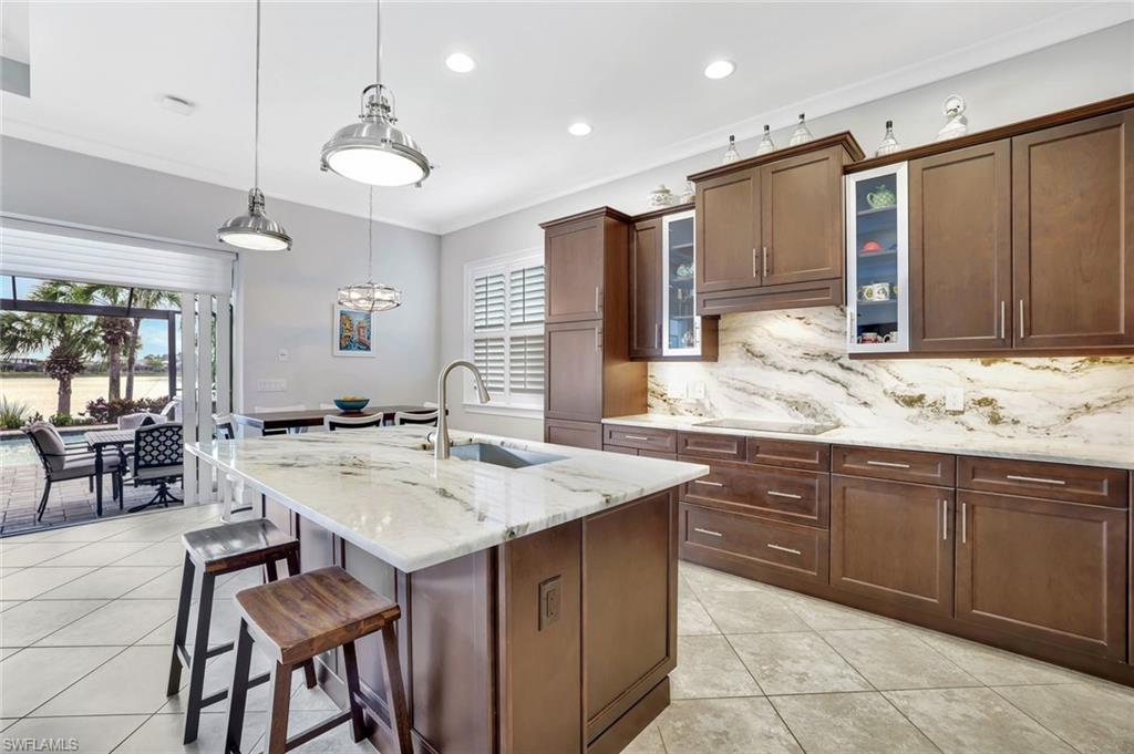 4905 Andros Drive Naples, FL 34113 - Photo 45 of 45 Kitchen featuring a island with seating and breakfast area, hanging light fixtures, glass insert cabinets, and crown molding