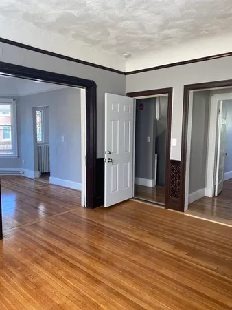 an empty room with wooden floor and way to kitchen