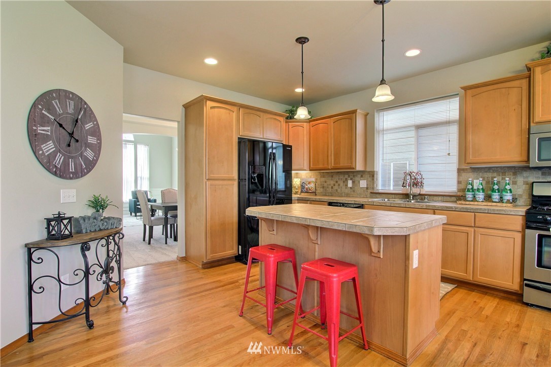 3827 160th Place Southeast Bothell, WA 98012 - Photo 13 of 40 a kitchen with stainless steel appliances granite countertop a stove a refrigerator a sink dishwasher a dining table and chairs with wooden floor