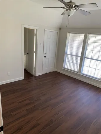 an empty room with wooden floor fan and windows