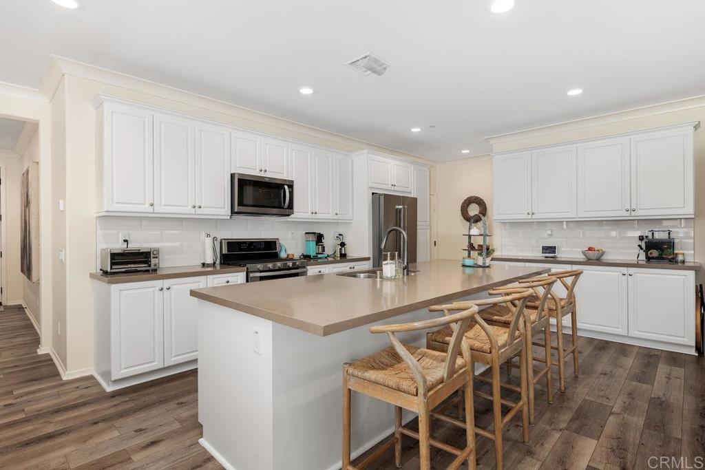 655 Merit Drive San Marcos, CA 92078 - Photo 7 of 35 a kitchen with stainless steel appliances granite countertop a stove top oven a sink a refrigerator and white cabinets with wooden floor