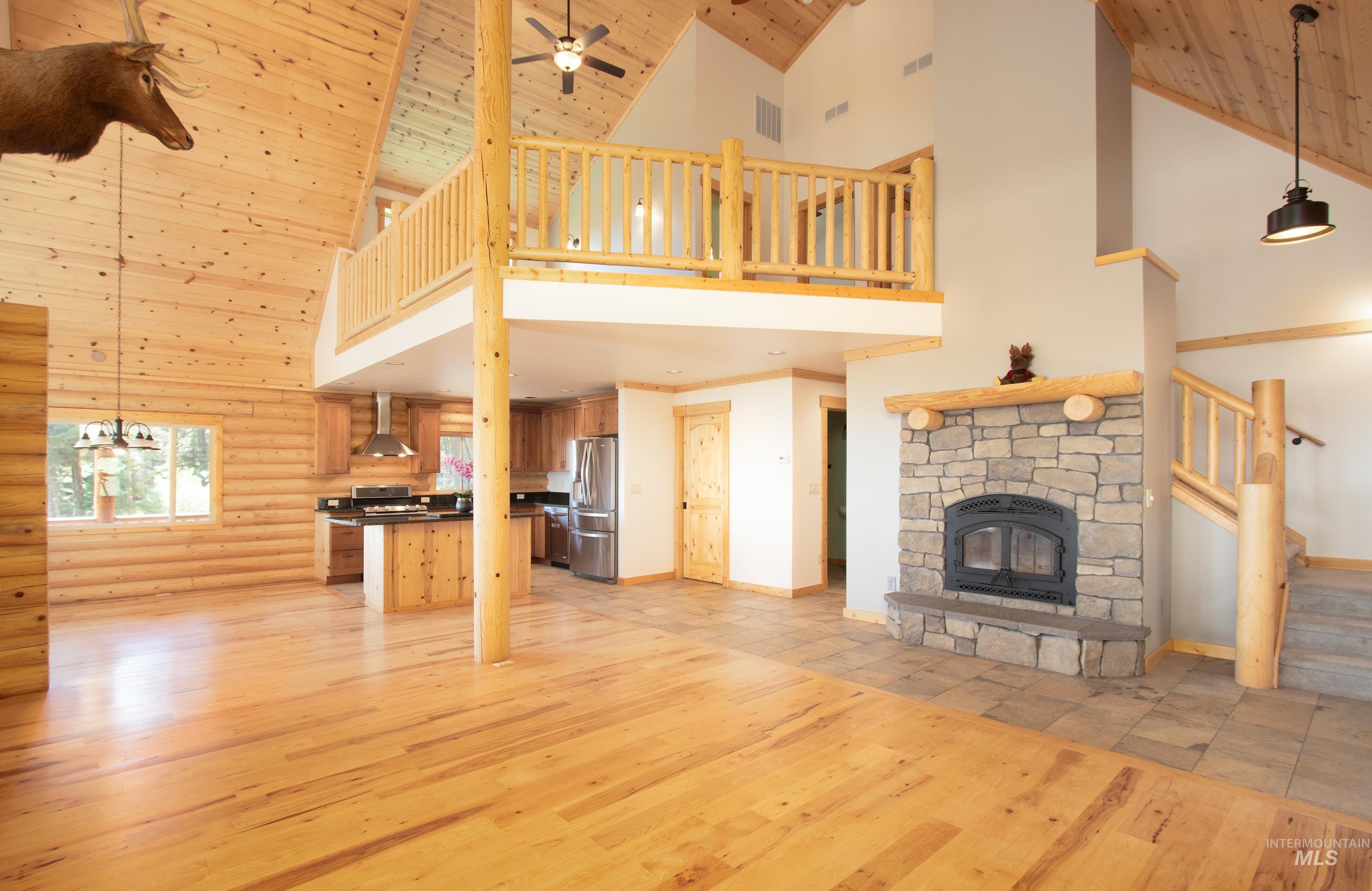 1539 West Mountain Road Cascade, ID 83611 - Photo 10 of 33 Unfurnished living room featuring light wood-style floors, rustic walls, a fireplace, a vaulted wood ceiling, and a ceiling fan