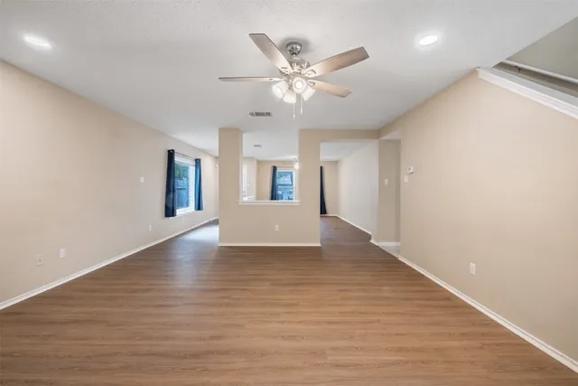 a view of an empty room with wooden floor and a ceiling fan