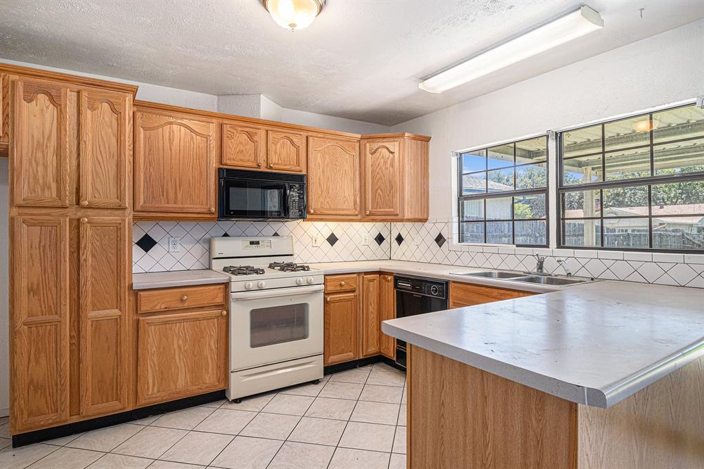 1814 Addington Drive Carrollton, TX 75007 - Photo 9 of 24 Kitchen with light tile floors, kitchen peninsula, black appliances, backsplash, and sink