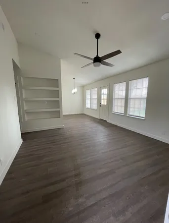 an empty room with wooden floor chandelier and windows