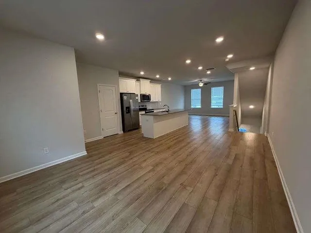 an empty room with wooden floor and kitchen view
