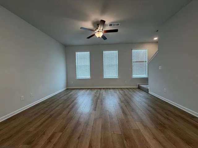 an empty room with wooden floor fan and windows