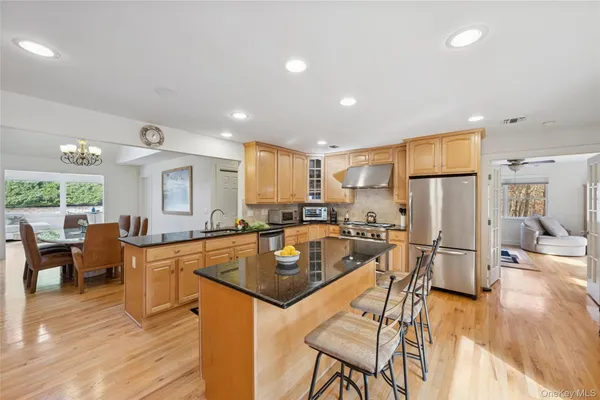 a kitchen with stainless steel appliances granite countertop a refrigerator oven a sink a dining table and chairs with wooden floor