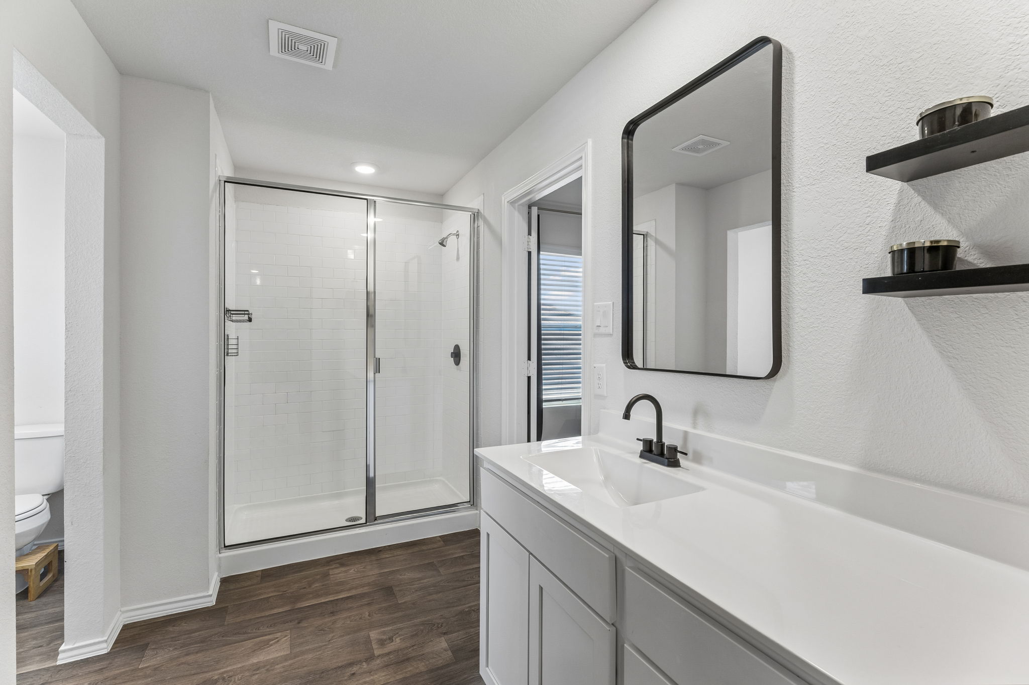 343 Sickle Loop Kyle, TX 78640 - Photo 26 of 40 Bathroom featuring a frameless glass shower enclosure with subway tile surround, white vanity with integrated sink and chrome faucet, rectangular mirror with black frame, and wood-finish flooring