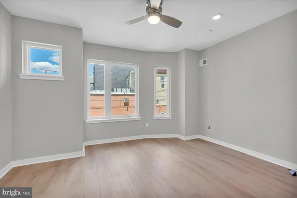an empty room with wooden floor chandelier fan and windows
