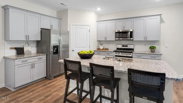 a kitchen with stainless steel appliances a stove a sink a refrigerator white cabinets and chairs