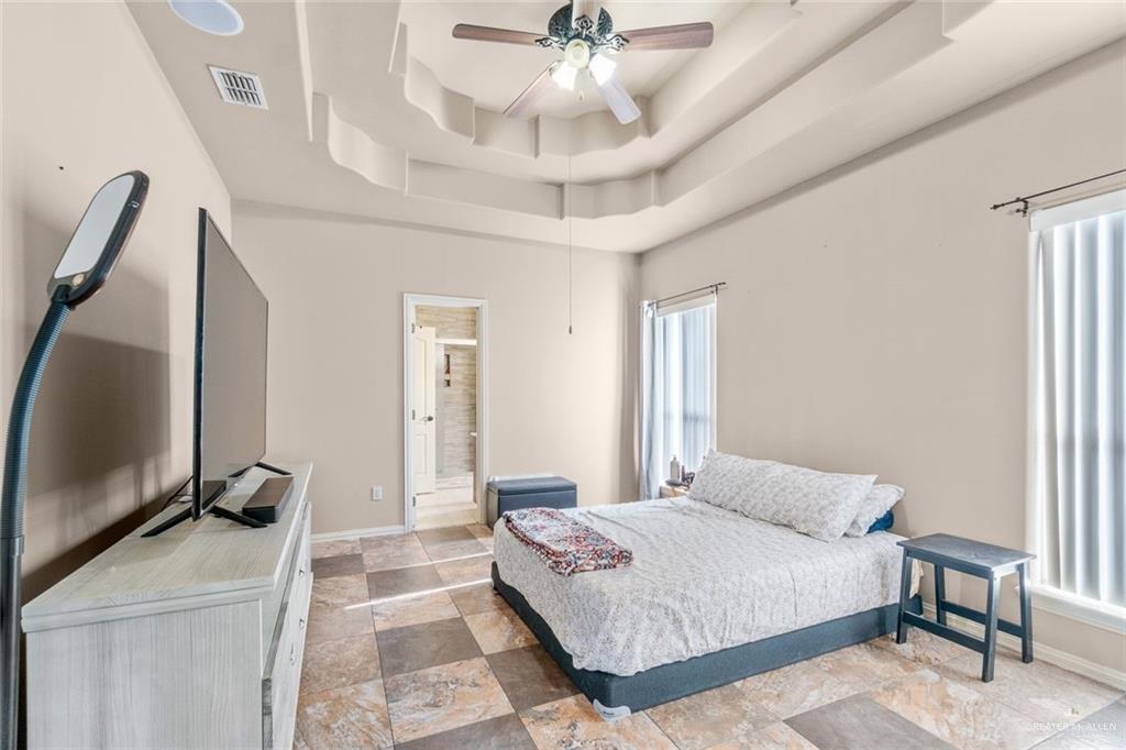2904 Victoria Street Hidalgo, TX 78557 - Photo 11 of 25 Bedroom with a tray ceiling, a ceiling fan, ensuite bathroom, and light stone finish floors