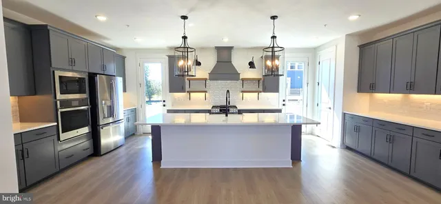 a kitchen with stainless steel appliances kitchen island granite countertop a refrigerator a stove and white cabinets with wooden floor