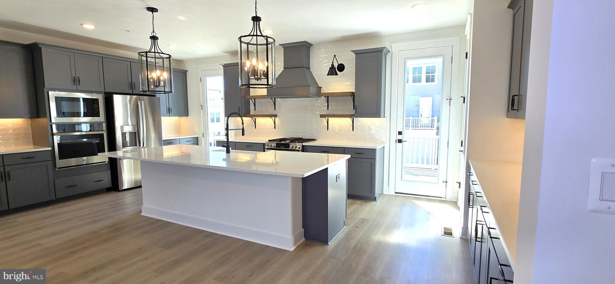 1726 Blacksmith Way Frederick, MD 21702 - Photo 12 of 64 a large kitchen with stainless steel appliances kitchen island granite countertop a refrigerator a sink dishwasher a stove and a dining table with wooden floor