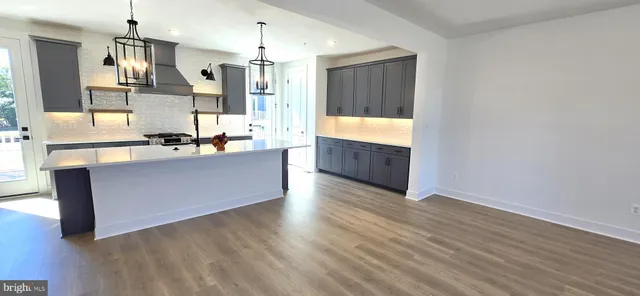 a large kitchen with stainless steel appliances kitchen island granite countertop a refrigerator a sink dishwasher a stove and a dining table with wooden floor