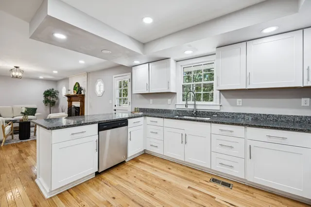 a kitchen with granite countertop white cabinets white appliances a sink and a window