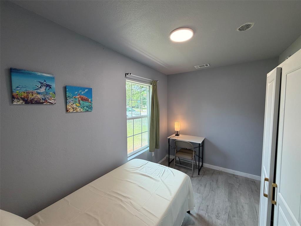 714 Southwest Dallas Street Grand Prairie, TX 75051 - Photo 17 of 27 Bedroom featuring light gray walls, wood-finish flooring, a window with exterior views, and a white built-in wardrobe with brass hardware