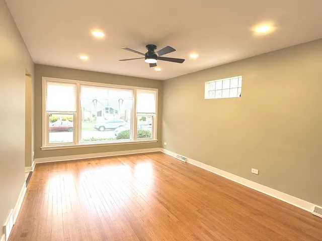 an empty room with wooden floor fan and windows