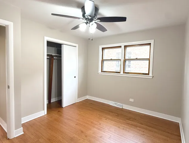 an empty room with wooden floor chandelier fan and windows
